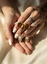Gros plan sur boucles d'oreilles dorées avec perle nacrée, portées par une femme avec tatouages, ambiance chaleureuse, style chic, SKU: 6mm